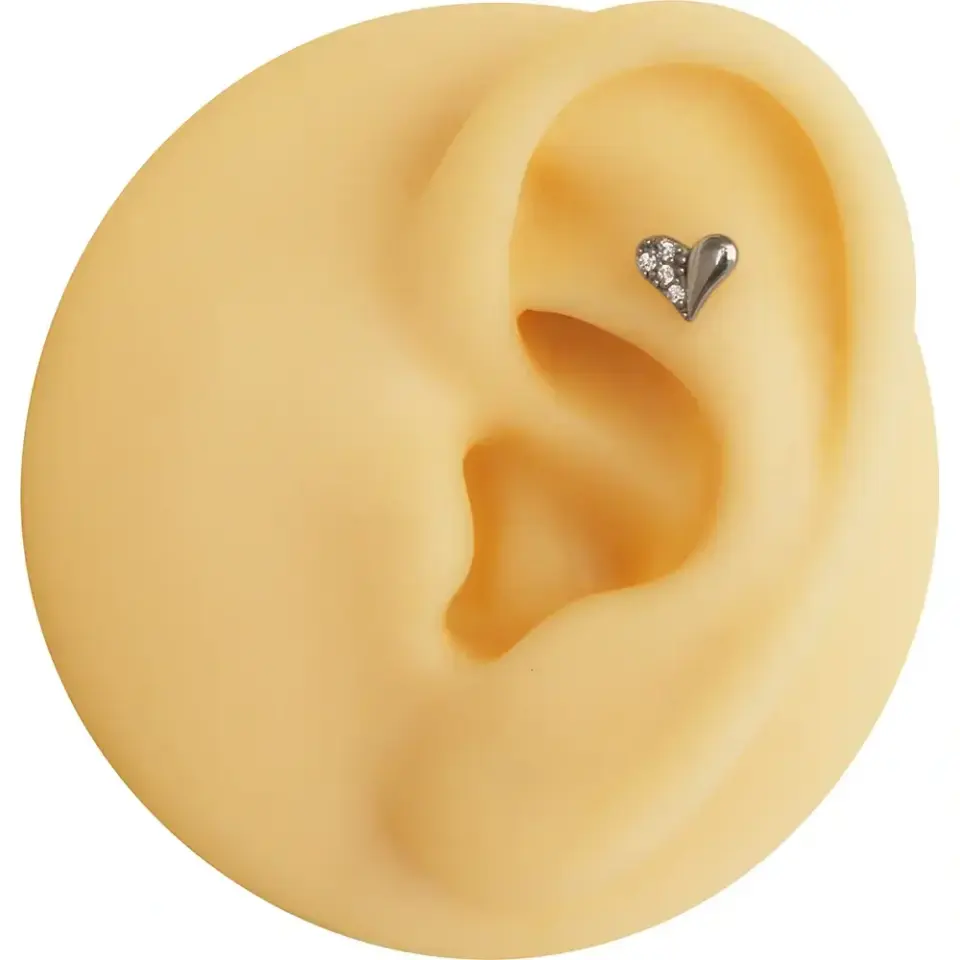 Helix bölgesinde modern bir duruş sergileyen gümüş renkli taşlı kalp kıkırdak piercing