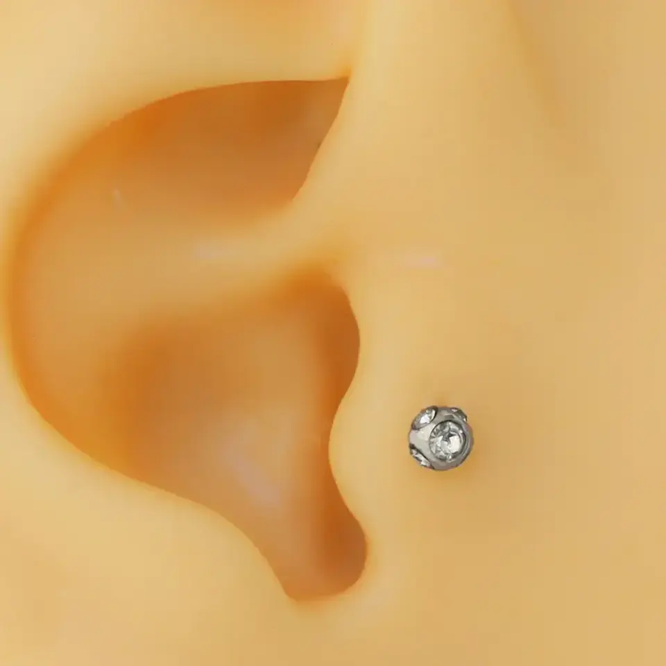 Kulak tragus ve kıkırdak bölgesinde parlayan disko taşlı gümüş piercing duruşu
