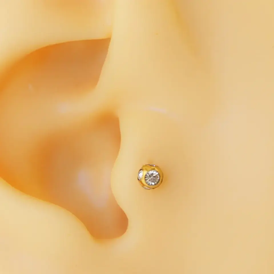Kulak tragus ve kıkırdak bölgesinde parlayan disko taşlı altın piercing duruşu