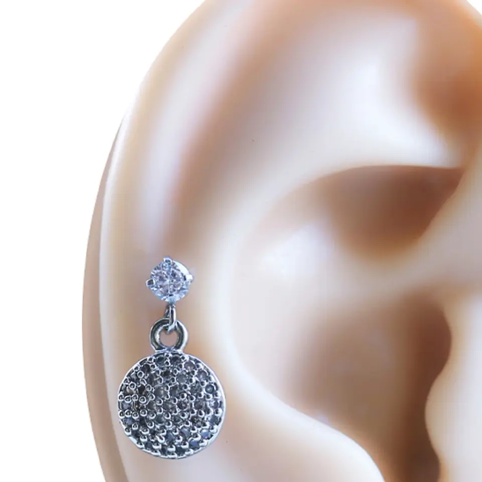 Kulakta sallantılı duruşuyla zirkon taşlı gümüş rengi tragus helix kıkırdak piercing.