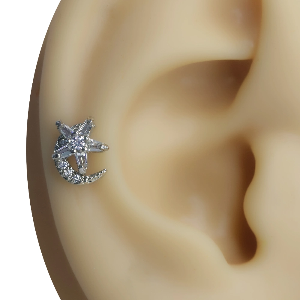 Kulak tragus ve helix bölgesinde sergilenen ay yıldız figürlü gece ışığı piercing.