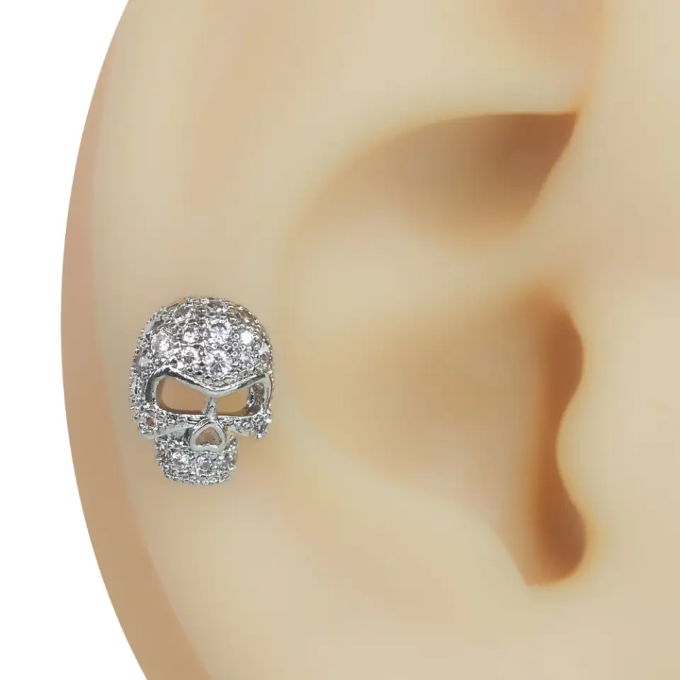 Kulak tragus ve helix bölgesinde sergilenen zirkon taşlı kurukafa figürlü gümüş renk piercing
