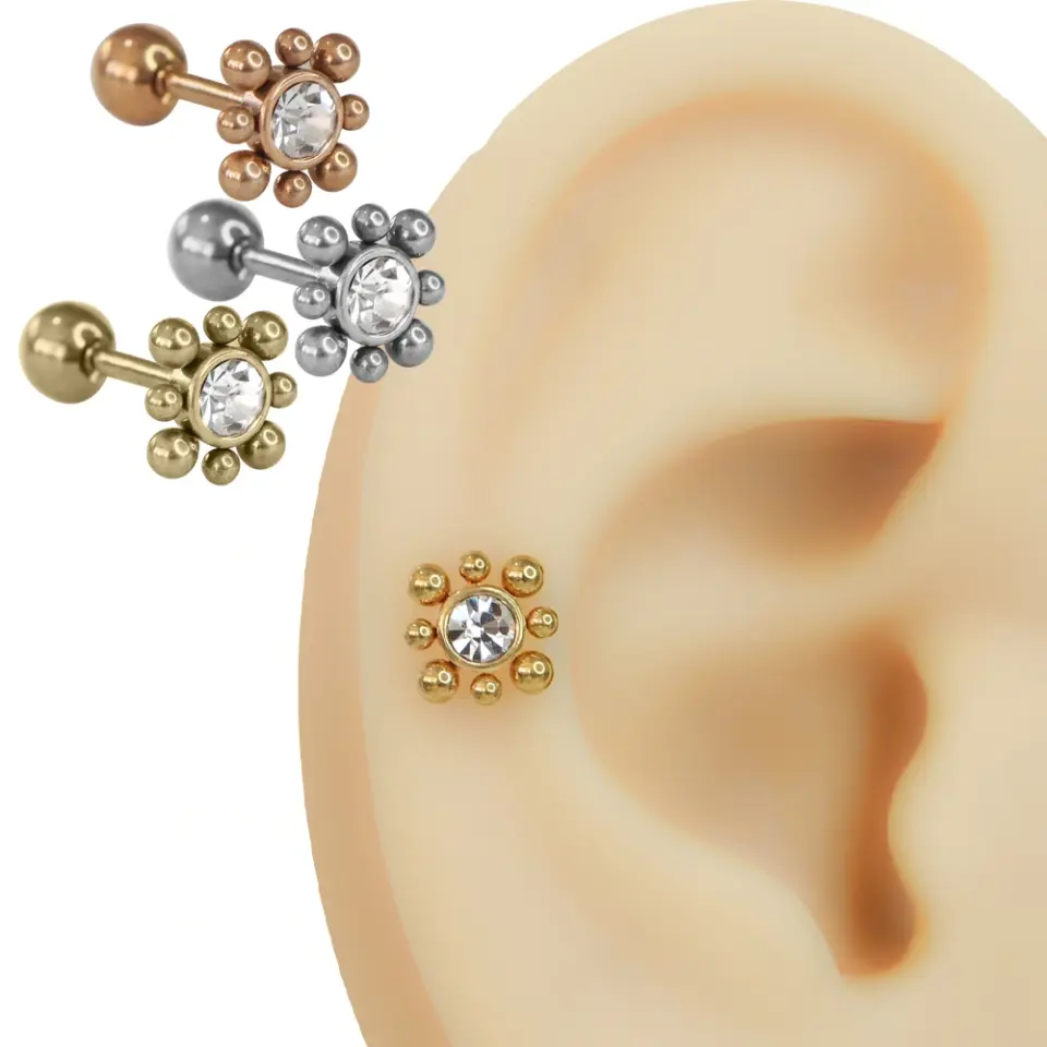 Kulakta helix piercing olarak takılmış, ortası parlak taşlı ve etrafı metal kürelerle çevrili çiçek tasarımlı cerrahi çelik piercing modeli