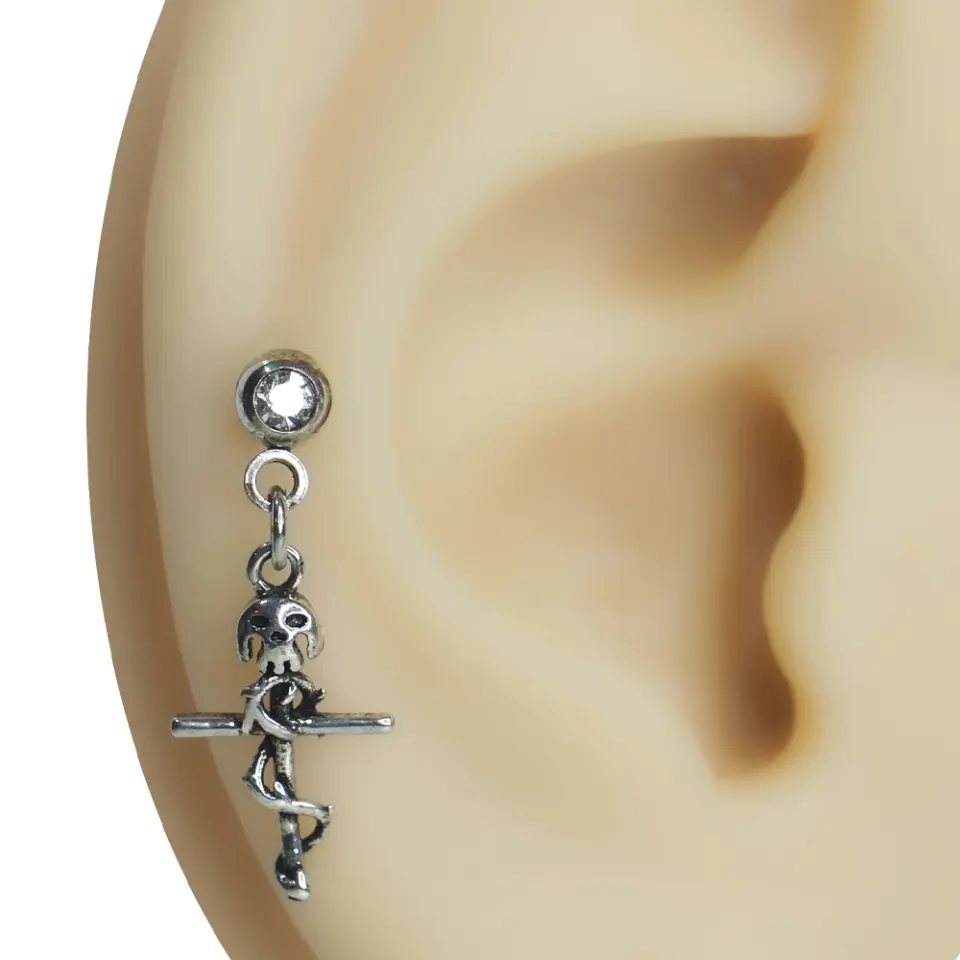 Kulakta sallantılı duruşuyla sergilenen zirkon taşlı kurukafa haç tragus helix kıkırdak piercing