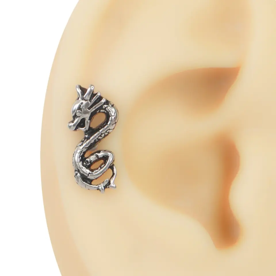 Kulak maketinin kıkırdak bölgesinde takılı, kıvrımlı gövdeye sahip gümüş renkli cerrahi çelik ejderha piercing