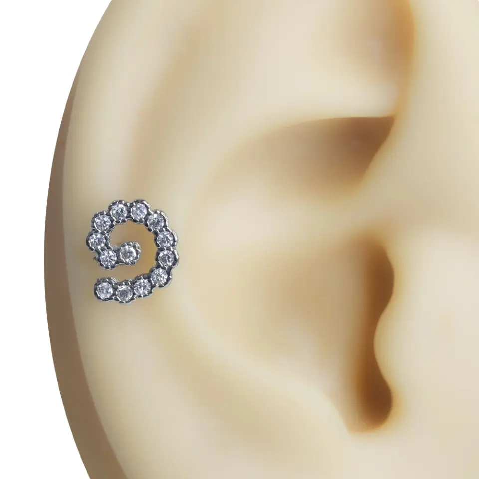 Kulak kıkırdağında sergilenen ışıltılı spiral formlu zirkon taşlı tragus helix kıkırdak piercing