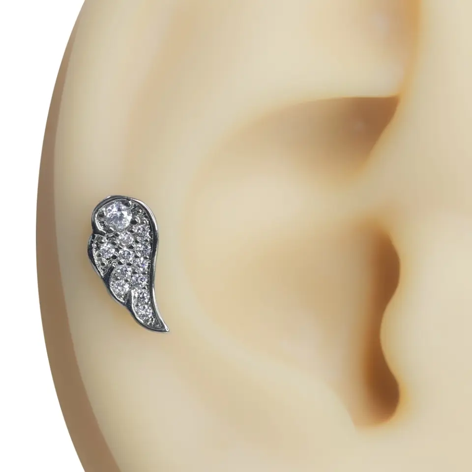 Kulak üzerinde sergilenen gümüş renkli melek kanadı formunda zirkon taşlı tragus helix kıkırdak piercing
