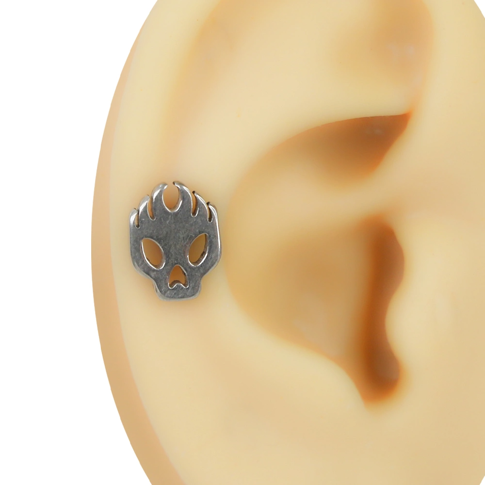 Kulakta helix kıkırdak bölgesinde takılı gümüş renkli alev detaylı kurukafa figürlü flatback piercing